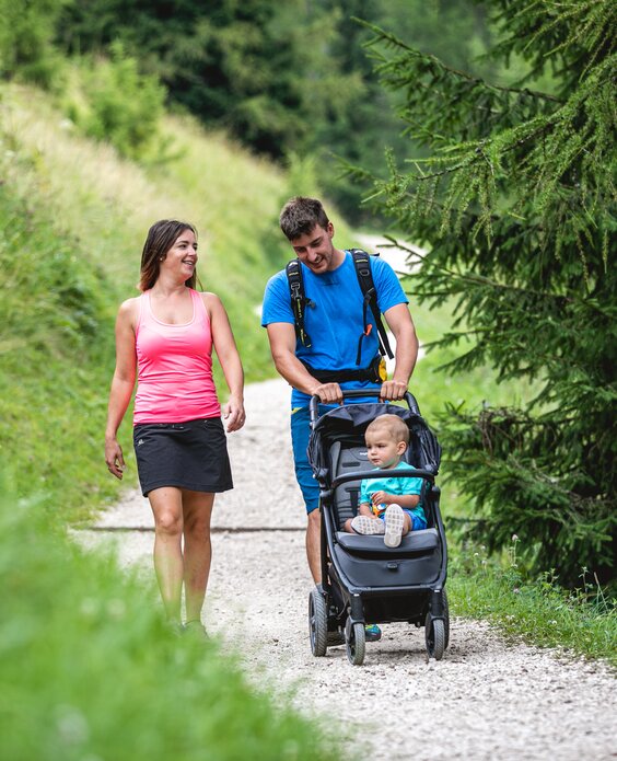 Genitori con passeggino camminano su strada sterrata a Latemar Dolomites | © APT Fiemme e Cembra - Alice Russolo