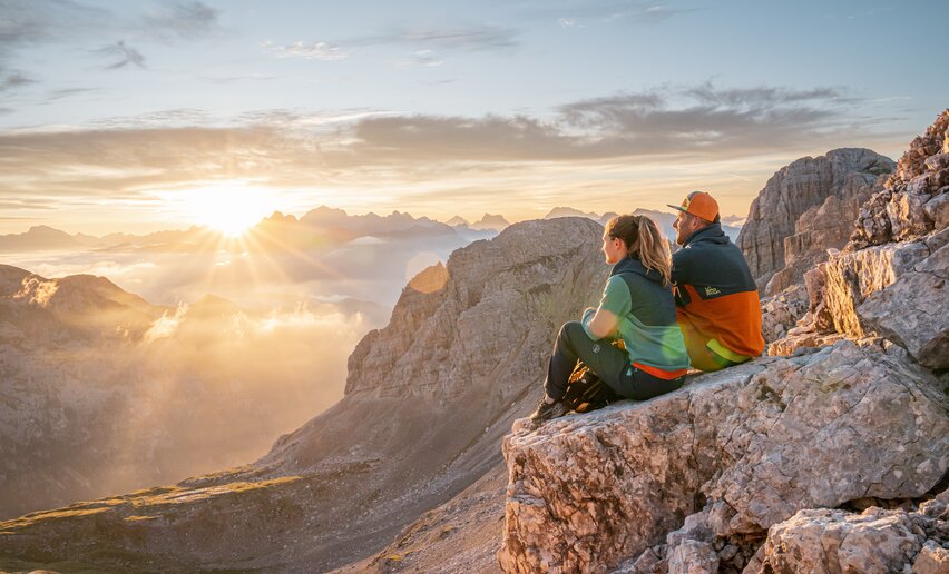 Coppia seduta su rocce ammira l'alba dal Latemar | © APT Fiemme e Cembra - Mattia Rizzi