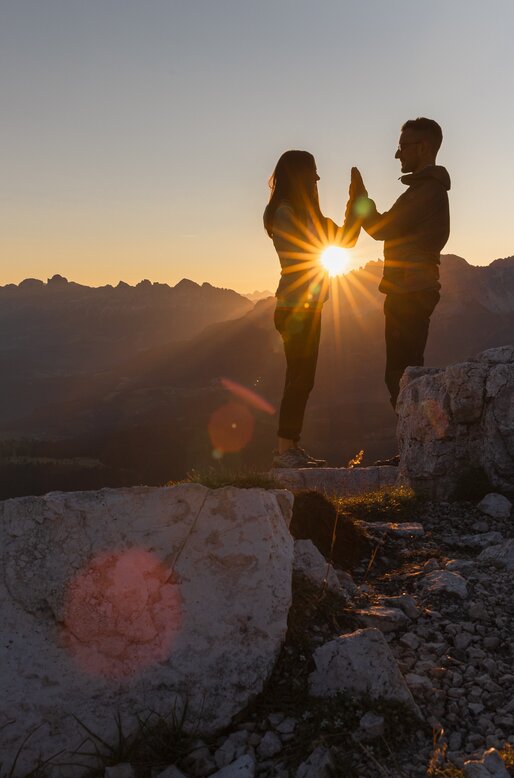 Coppia all'alba in montagna; i raggi del sole passano tra le loro mani giunte | © APT Fiemme e Cembra - foto di Gaia Panozzo