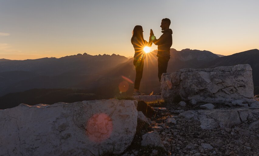 Coppia all'alba in montagna; i raggi del sole passano tra le loro mani giunte | © APT Fiemme e Cembra - foto di Gaia Panozzo