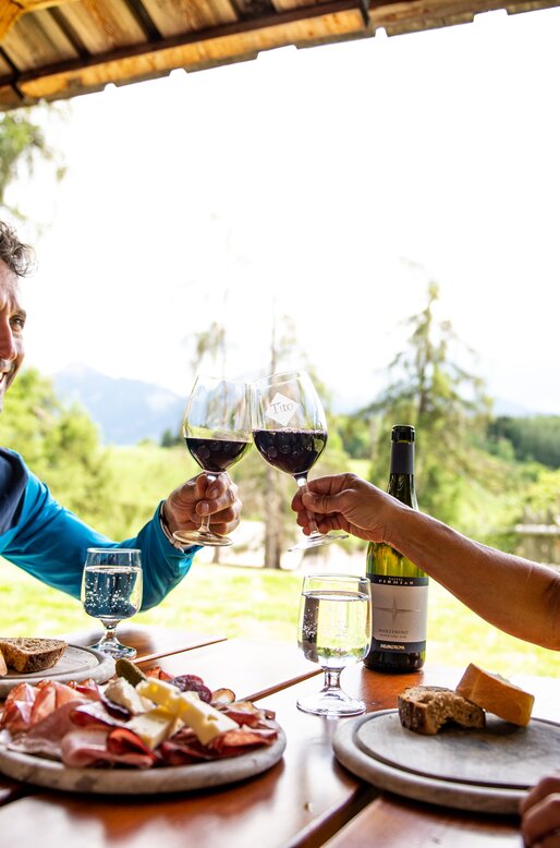 Coppia fa aperitivo in un tavolo all'aperto con tagliere misto e vino rosso | © 	 APT Fiemme e Cembra